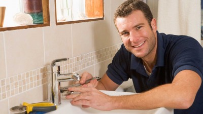 A smiling man repairing a sink faucet with tools nearby.