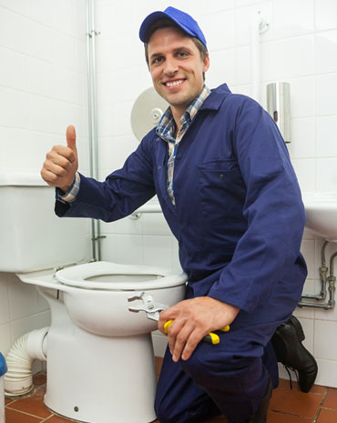 Plumber giving a thumbs-up next to a toilet he is presumably working on.