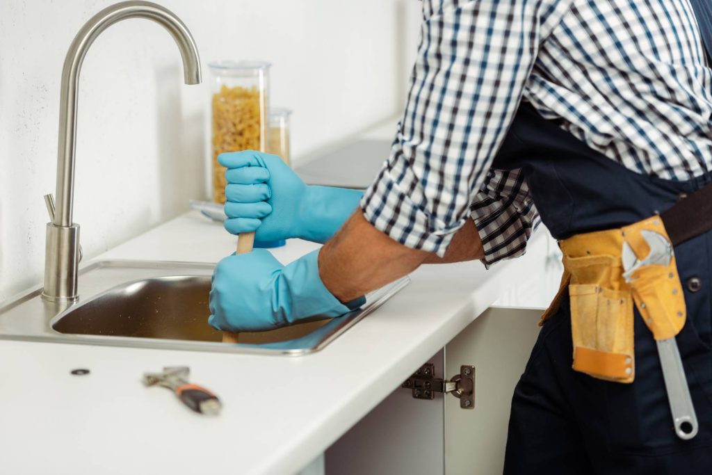 Plumber wearing gloves fixing a sink.