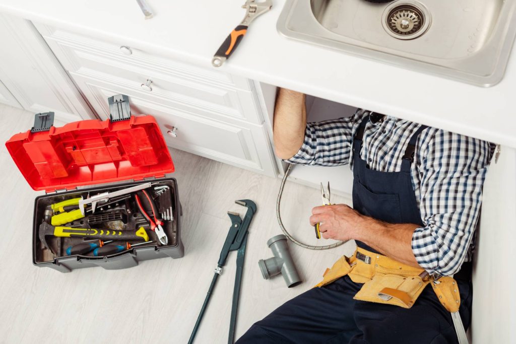 Plumber working under a kitchen sink with tools nearby.