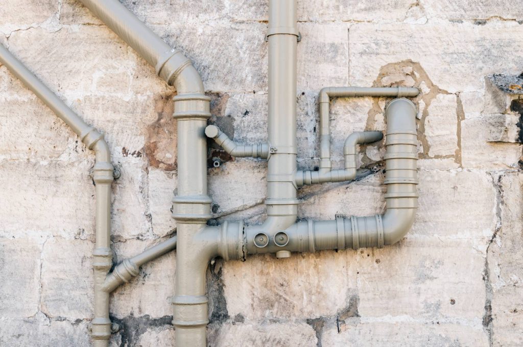 Complex network of gray pipes running along a concrete wall.