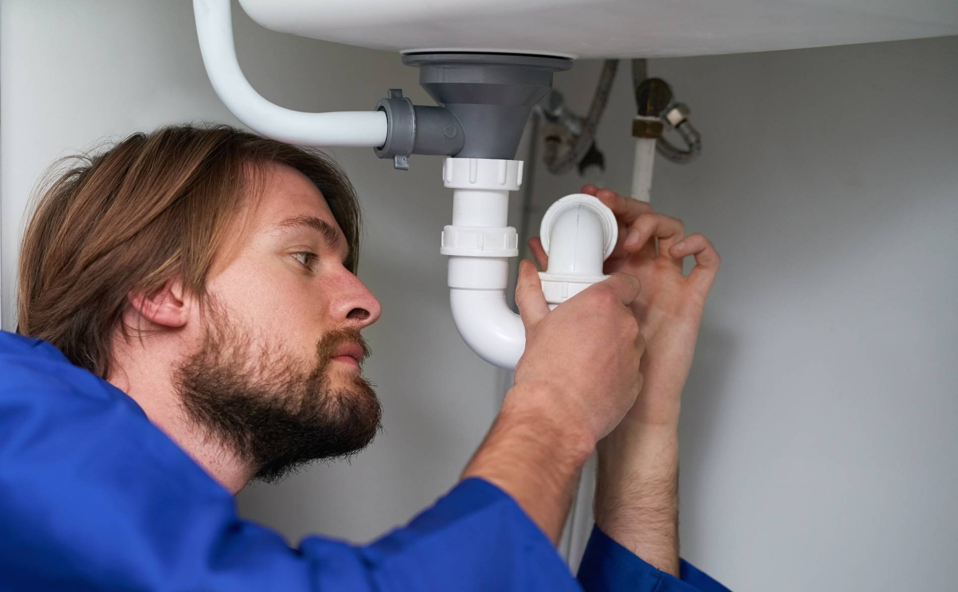 A plumber fixing the piping under a sink.